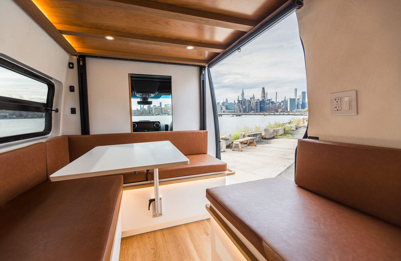 Interior workspace and meeting area of a custom Sprinter build, city skyline through the open side door